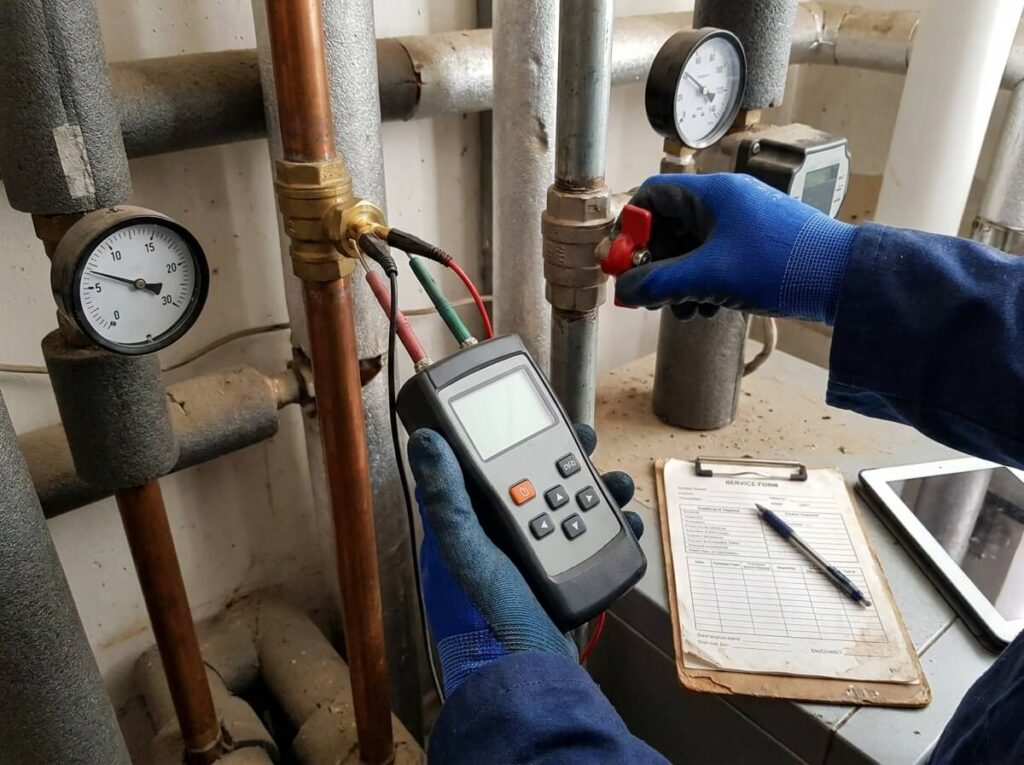 Heizungsinstallateur misst Temperatur und Betriebswerte an Heizungsrohren